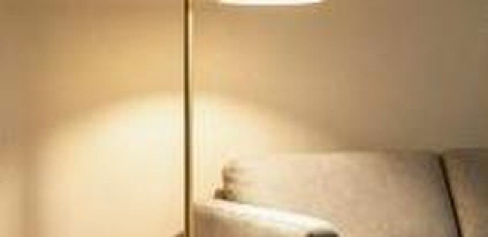 Luminária de piso dourada com cúpula em tecido ao lado de um sofá