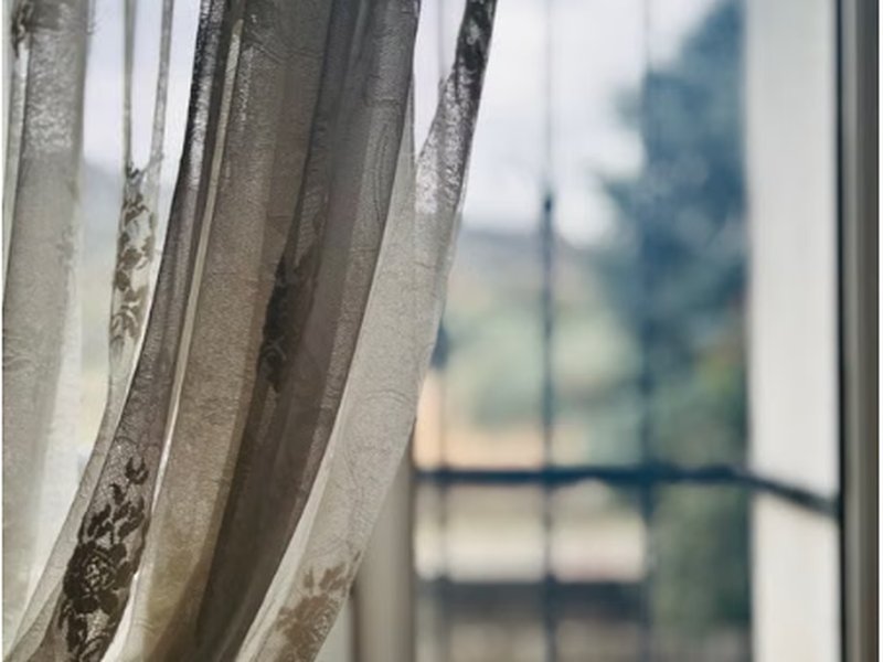 Cortina de tecido leve balançando ao lado de janela de cozinha