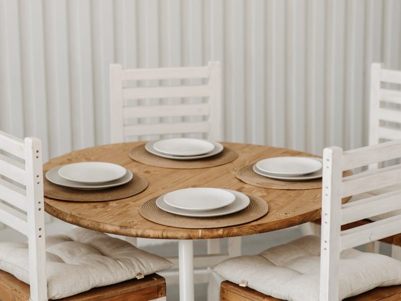 Mesa de cozinha redonda posta com pratos brancos e cadeiras claras ao redor