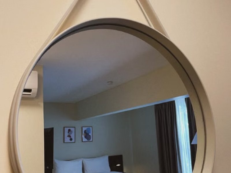 Espelho redondo decorativo com alça refletindo cama do quarto