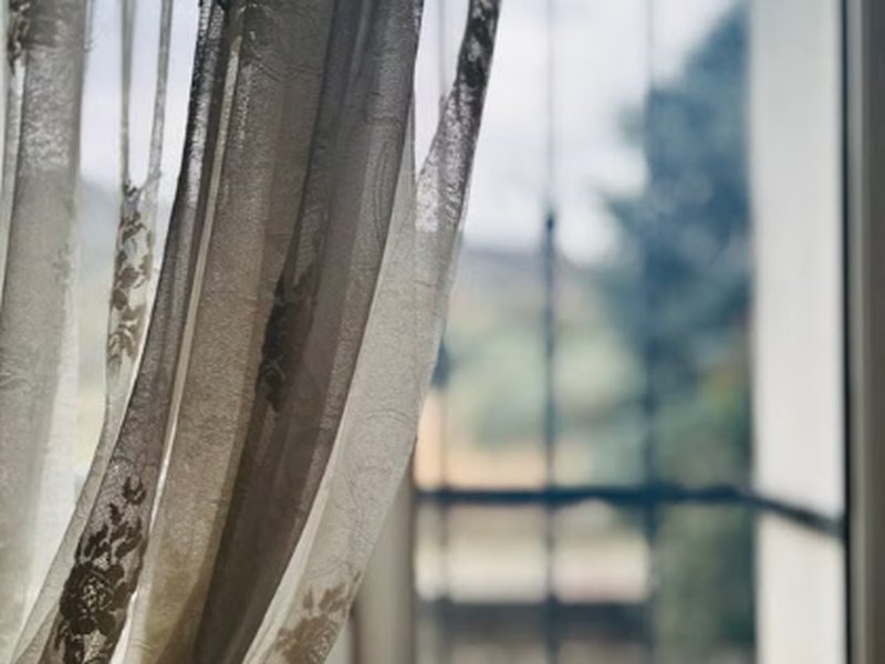 Cortina de tecido leve balançando ao lado de janela iluminada