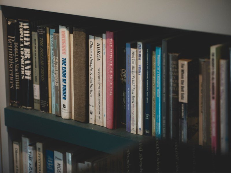 Detalhe de livros organizados lado a lado em uma prateleira de estante